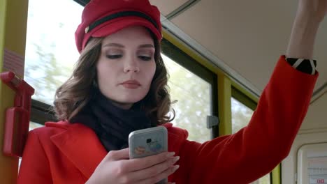 Portrait-of-an-elegant-young-girl-in-a-red-coat.-Uses-a-smartphone-in-public-transport.-Prints-a-text-message-on-the-bus