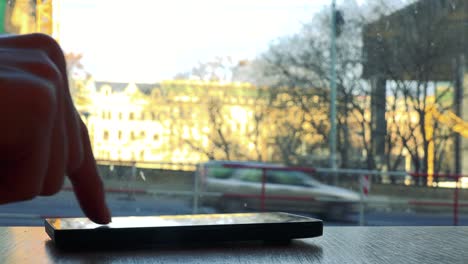 A-woman-works-on-a-smartphone-laid-on-a-table-in-a-cafe---closeup-on-the-phone,-a-window-in-the-background