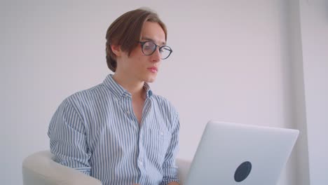 Closeup-portrait-of-young-attractive-caucasian-businessman-working-on-the-laptop-sitting-in-the-armchair-indoors