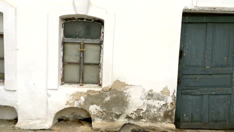 Weathered-and-damaged-wall-of-old-house,-plaster-white-with-damage-and-cracks.