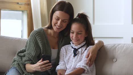 Mum-and-kid-daughter-using-smartphone-taking-selfie-on-sofa