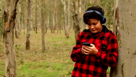 Adolescente-niño-con-auriculares-usando-teléfono-inteligente-en-la-naturaleza