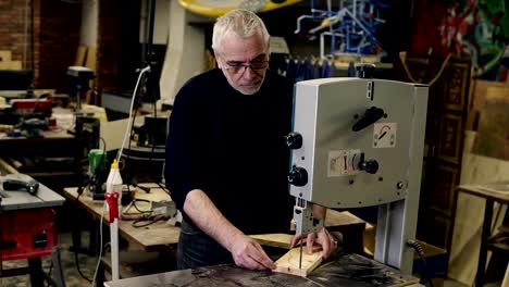 Portrait-of-an-adultgrey-haired-man-working-with-milling-machine-while-carving-a-wooden-pattern-in-a-working-room-at-workshop-.-Action.-Woodworking-industry