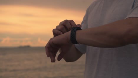 Nahaufnahme-asiatischen-Athleten-Läufer-Überprüfen-Herzfrequenz-auf-Smartwatch-nach-dem-Laufen-während-des-Stehens-am-Strand-während-eines-schönen-Sonnenuntergangs-im-Sommer.