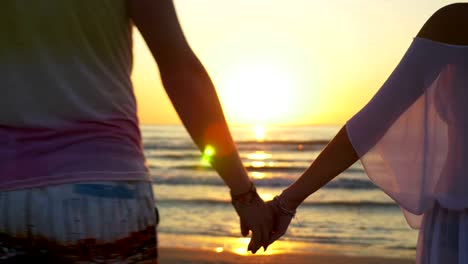 Romantic-couple-holding-hands-and-walking-towards-the-water-on-sandy-beach