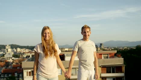 CLOSE-UP:-Happy-man-and-smiling-woman-standing-on-rooftop-raising-hands