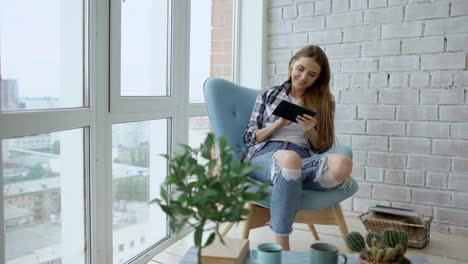 Mujer-atractiva-con-tableta-digital-sentado-en-silla-en-el-balcón-en-Apartamento-moderno-tipo-loft