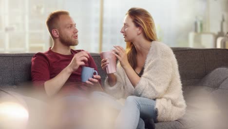 Junger-Freund,-ein-Hauch-von-seiner-Freundin-beim-Teetrinken-auf-der-Couch-entfernen