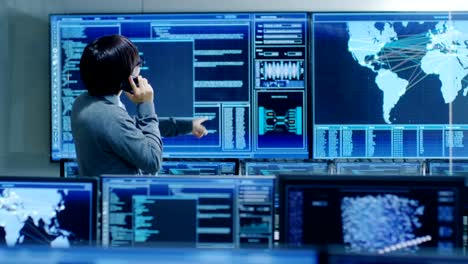 In-the-System-Control-Room-IT-Administrator-Talks-on-the-Phone.-He's-in-a-High-Tech-Facility-That-Works-on-the-Surveillance,-Neural-Networks,-Data-Mining,-AI-Projects.