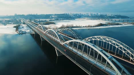 Auto-und-Zug-bewegt-sich-auf-einer-Brücke-über-einen-gefrorenen-Fluss-Luftbild-Drohne-Filmmaterial