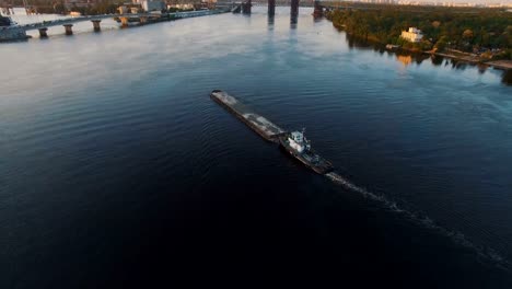 Barge-sails-along-the-river-near-the-city-port-on-sunset-aerial-footage