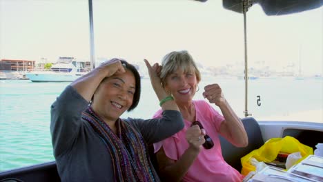 older-caucasian-and-asian-women-being-silly-and-having-fun-on-a-boat