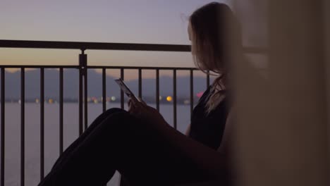 Frau-mit-Smartphone-auf-dem-Balkon-mit-Blick-auf-Meer