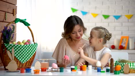 Niña,-tratando-de-pintar-huevos-de-Pascua,-madre-cariñosa-ayuda-y-apoyándola