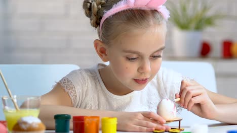 Diligent-girl-carefully-putting-pattern-with-paints-on-egg,-Easter-decoration