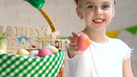 Little-girl-decorating-egg-with-paint,-Easter-greeting-basket-standing-on-table