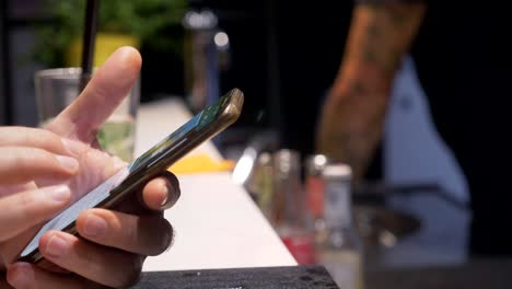 caucasian-man's-hands-surfing-on-smartphone-at-bar-counter--close-up