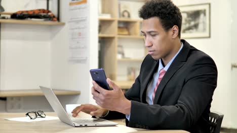 African-Businessman-Using-Phone-and-Laptop-for-information