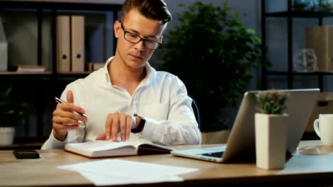 Junge-Geschäftsleute,-die-Laptop-verwenden,-notieren-etwas-im-Notizbuch,-während-sie-am-Abend-im-Büro-arbeiten.