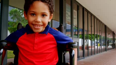 Front-view-of-happy-disabled-African-American-schoolboy-sitting-on-wheelchair-in-school-corridor-4k