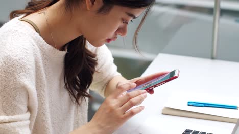 pretty-young-asian-woman-using-mobile-phone-and-laptop-indoor