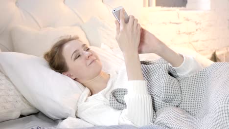 Junge-Frau-mit-Smartphone-beim-Liegen-im-Bett