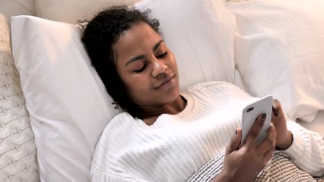 Top-View-of-African-Woman-Using-Smartphone-while-Relaxing-in-Bed