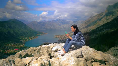 Middle-Aged-Woman-sitting-on-top-of-mountain-and-talking-by-smartphone