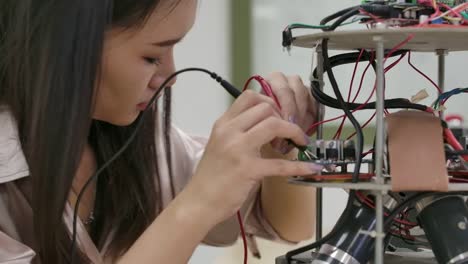 Asian-female-electronics-engineer-works-with-robot,-building,-fixing-robotics-in-workshop.-People-with-technology-or-innovation-concept.