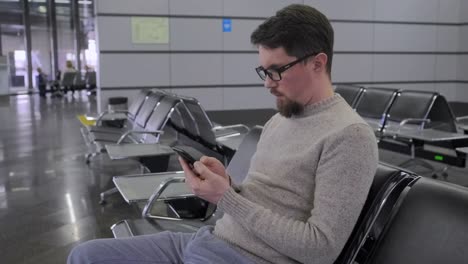 Mann-scrollt-Bildschirm-des-Smartphones-in-der-Abflug-Lounge