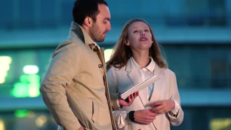 Two-young-work-colleagues-using-a-digital-tablet-while-standing-together-outside-late-at-night