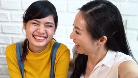 Happy-Asian-teenage-daughter-and-middle-aged-mother-taking-selfie-or-video-calling