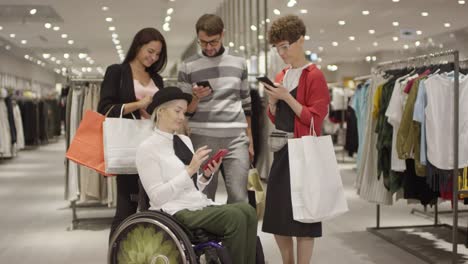 Diverse-Group-of-Friends-Looking-at-Phone-in-Clothes-Store