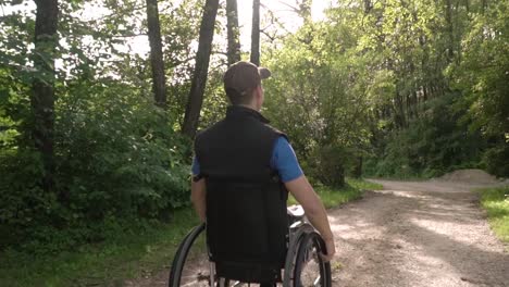 Slowmotion-back-follow-of-disabled-young-student-man-in-a-wheelchair-observing-nature-around-him,-with-sun-flare