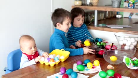 Three-children,-coloring-and-painting-easter-eggs-at-home-for-the-holiday