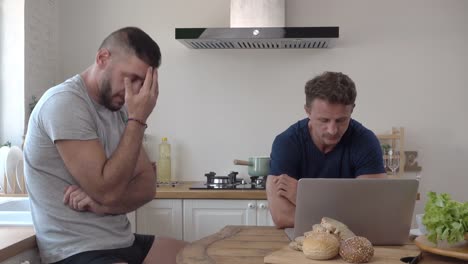 Gay-male-couple-acting-concerned-impatient-and-frustrated-at-kitchen-table