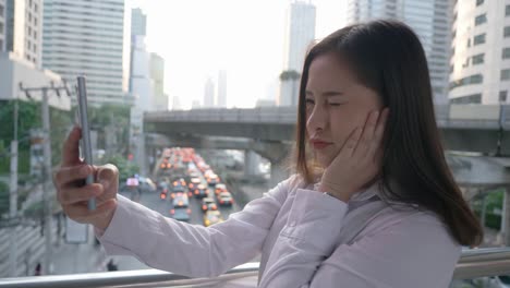 Beautiful-Young-smiling-asian-woman-taking-cell-phone-photos--in-the-modern-city-center-in-the-evening-of-Bangkok-Thailand.