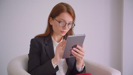 Nahaufnahme-Porträt-der-jungen-kaukasischen-Geschäftsfrau-in-Brille-SMS-auf-dem-Tablet-sitzen-deiner-Sessel-in-der-weißen-Wohnung