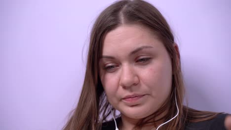 Young-girl-with-serious-face-and-poor-eyesight-squints-to-read-or-to-see-something-on-smartphone-screen,-scratches-her-nose-and-talks-on-mobile-phone-using-headset,-close-up