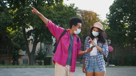 Afro-american-man-in-protective-mask-is-asking-woman-the-right-way,-showing-map-on-smartphone