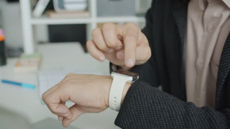 Close-up-of-male-hand-touching-electronic-watch-screen-using-modern-device-in-office