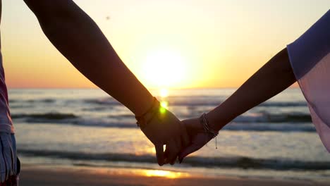 Junges-Paar-Hand-in-Hand-am-Strand-bei-Sonnenuntergang-