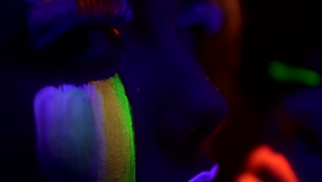 Detailansicht-der-beiden-schönen-Mädchen-mit-fluoreszierenden-Make-up-unter-UV-Schwarzlicht-gegenseitig-streicheln-und-küssen.-Slowmotion-Aufnahme