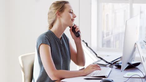 Young-white-woman-using-phone-and-computer-in-an-office