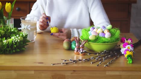 Frau-malt-ein-gelbes-Ei-auf-dem-Tisch-mit-Osterschmuck