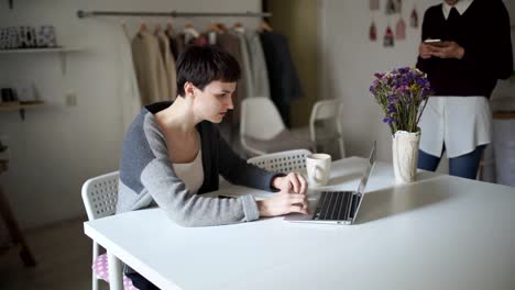 Mujer-joven-sentada-en-la-mesa-y-escribiendo-en-la-laptop.-Mujer-con-el-teléfono-inteligente