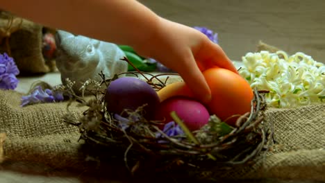 Child's-hand-lays-colored-egg-in-in-the-Easter-nest