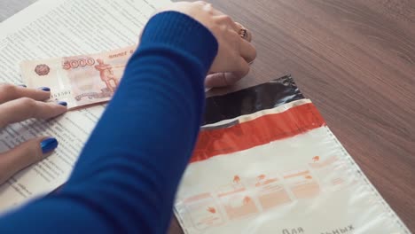 Woman-hands-puts-pile-of-ruble-banknotes-money-into-plastic-envelope