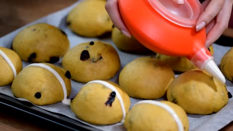 Raw-unbaked-buns.-Ready-to-bake-homemade-Easter-traditional-hot-cross-buns-on-baking-paper.-Female-hands-make-a-cross.