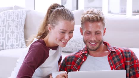 Joven-pareja-blanca-sentada-en-el-suelo-en-casa-utilizando-la-computadora-portátil